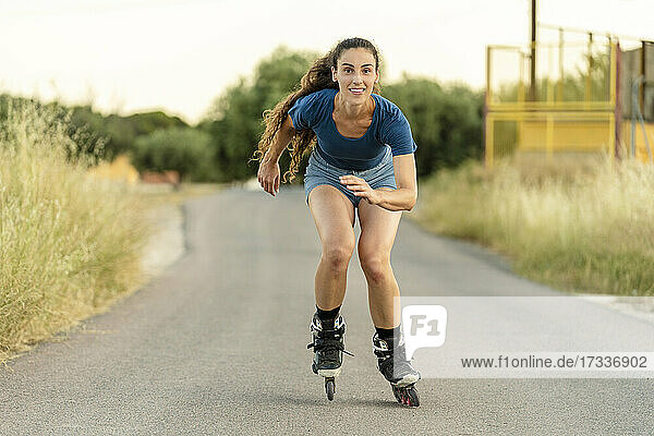 Lächelnde junge Frau beim Rollschuhlaufen auf der Straße