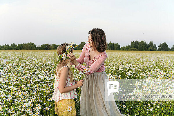 Mother making flower tiara for daughter while standing in field