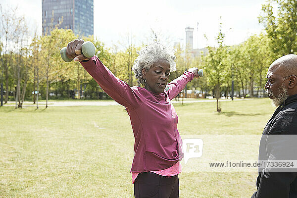 Mann schaut auf ältere Frau  die mit Hanteln im Park trainiert