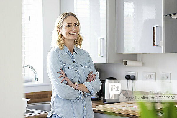 Woman with arms crossed standing in kitchen at home