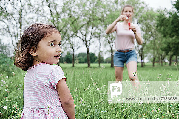 Tochter schaut weg  während die Mutter im Park im Gras steht