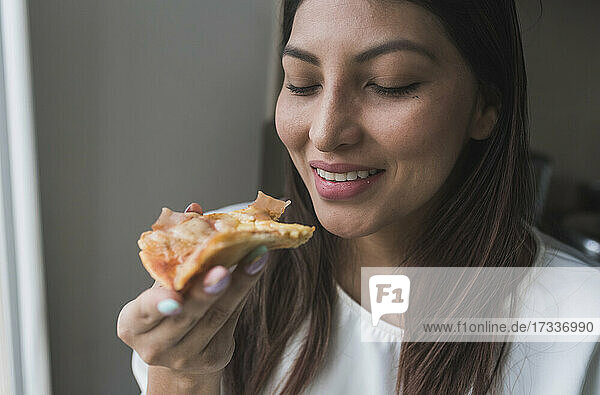 Lächelnde Frau hält Pizzastück zu Hause