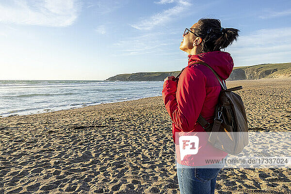 Frau mit Rucksack genießt die Einsamkeit am Strand bei Sonnenuntergang