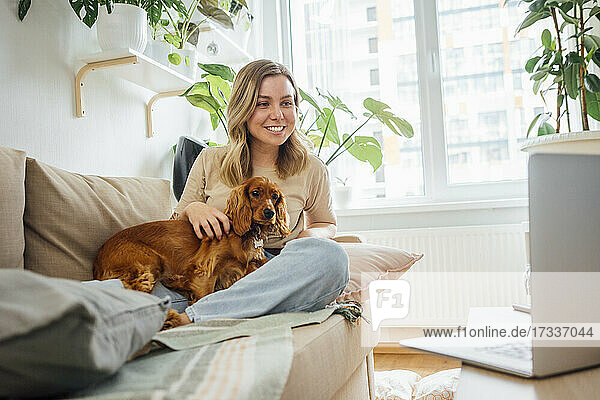 Smiling businesswoman stroking dog during video conference through laptop at home