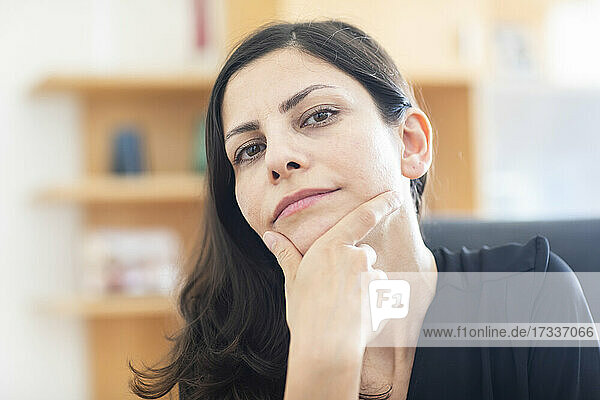 Geschäftsfrau sitzend mit Hand am Kinn im Büro
