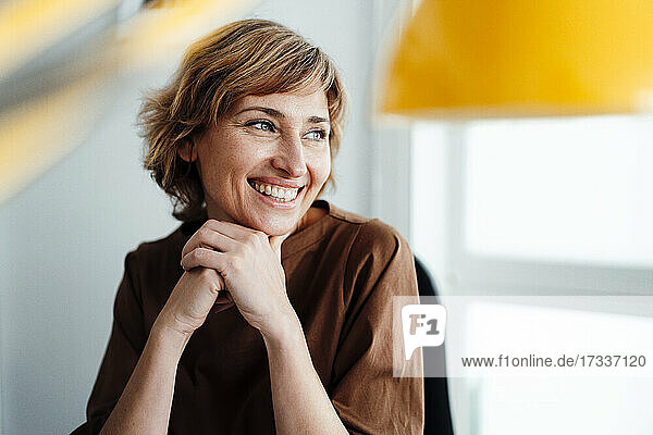Smiling businesswoman with hand on chin looking away in office
