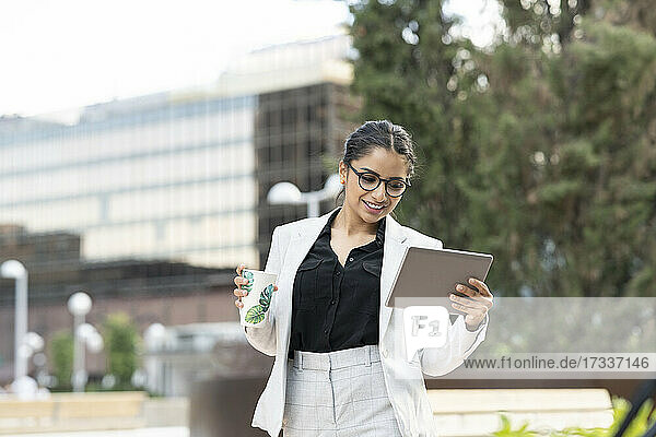 Female professional holding disposable cup while using digital tablet in office park