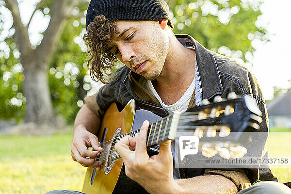 Hübscher junger Mann spielt Gitarre im Park