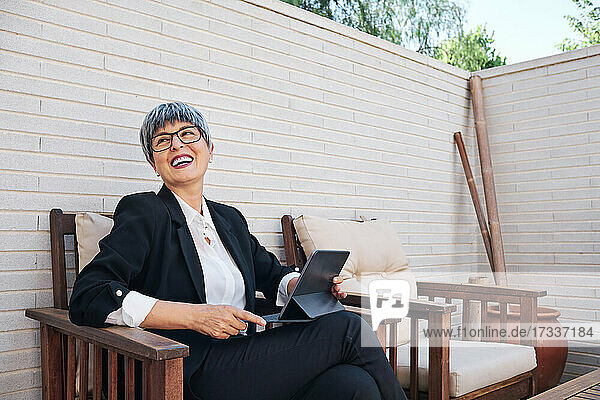 Businesswoman laughing and looking away while sitting on chair in backyard