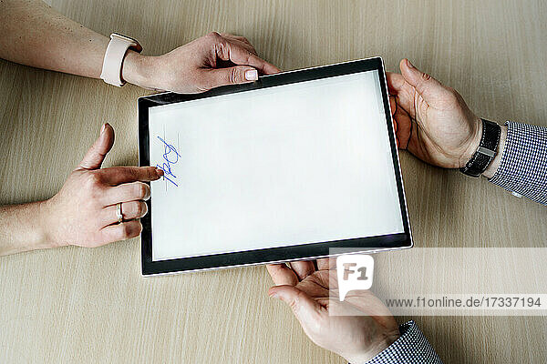 Geschäftsfrau  die eine Unterschrift leistet  während ein Geschäftsmann ein digitales Tablet am Schreibtisch im Büro hält