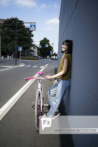 Frau lehnt sich an die Wand und hält ein Fahrrad