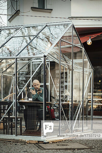 Male cafe owner sitting in glass cabinet