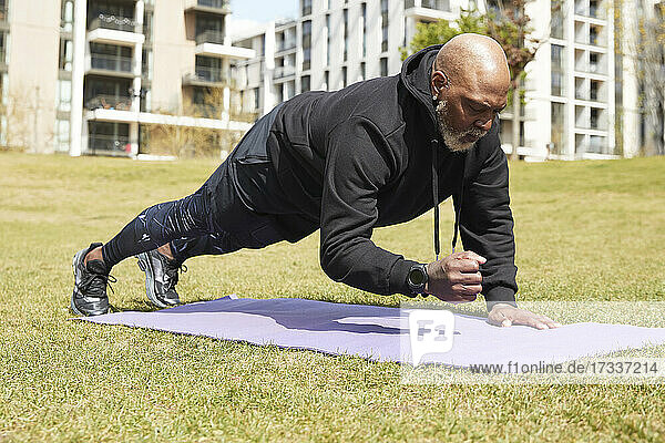 Man practicing plank position on exercise mat in public park