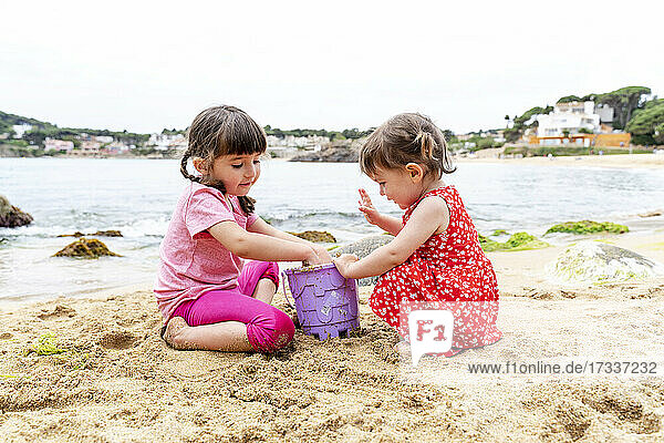 Girls putting sand in bucket at beach