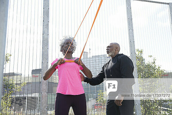 Mann hilft Frau beim Training mit Widerstandsbändern im Park an einem sonnigen Tag