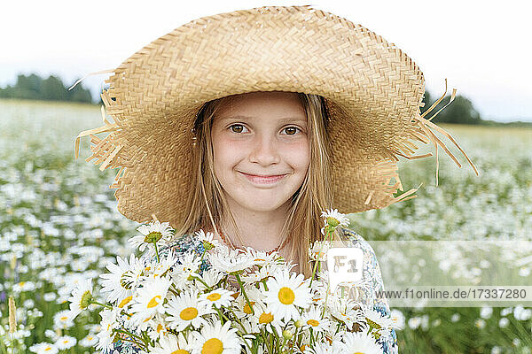 Lächelndes Mädchen mit Hut und Blumen auf einem Feld