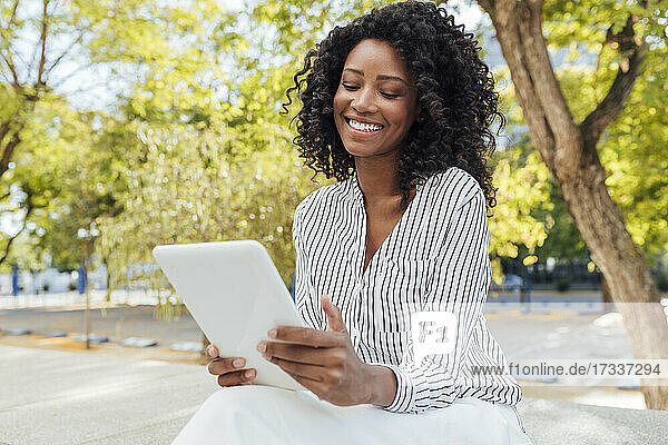 Fröhliche weibliche Fachkraft  die ein digitales Tablet benutzt  während sie im Büropark sitzt