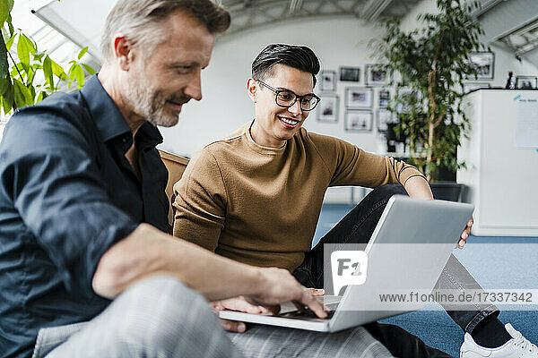 Männlicher Berufstätiger  der einen Laptop benutzt  während er neben einem Kollegen im Kreativbüro sitzt