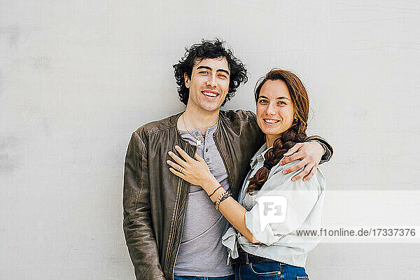 Smiling couple standing together in front of white wall
