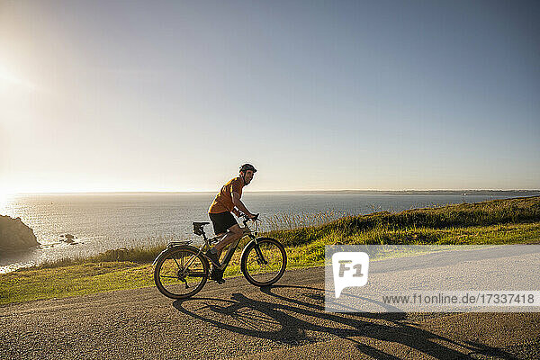 Mature male athlete cycling on road at sunset