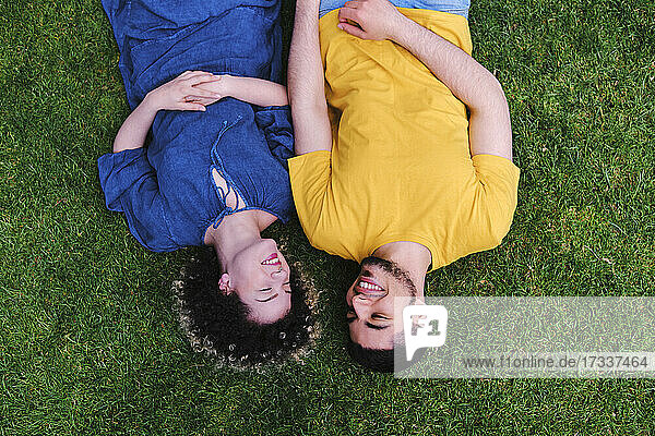 Lächelndes junges Paar  das zusammen auf dem Rasen eines Parks liegt