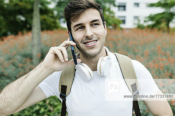 Lächelnder junger Mann  der wegschaut  während er mit seinem Smartphone telefoniert
