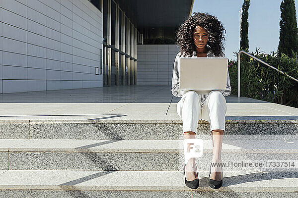 Berufstätige Frau  die einen Laptop benutzt  während sie an einem sonnigen Tag auf einer Treppe sitzt