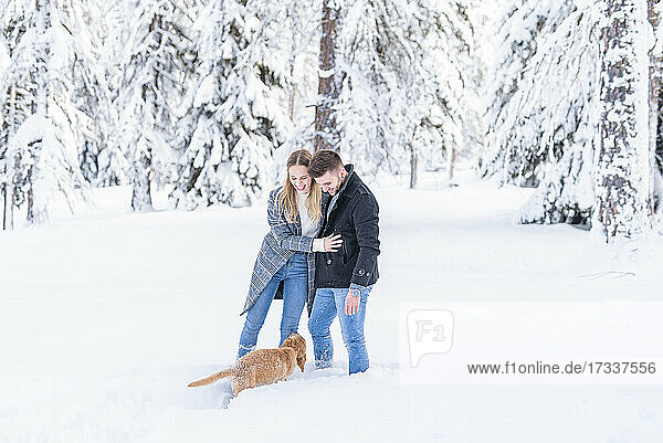 Young couple standing in snow with dog during vacation