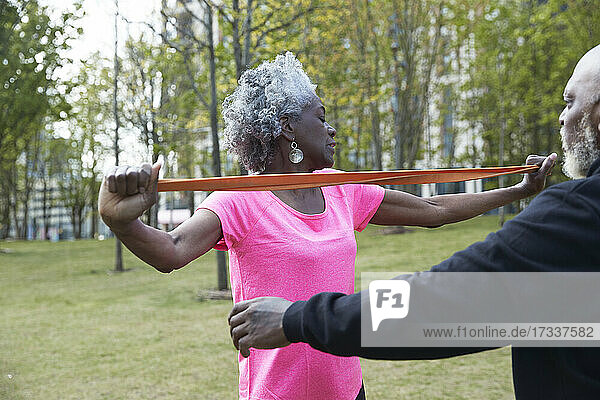 Mann hilft Frau beim Training mit Widerstandsband im Park