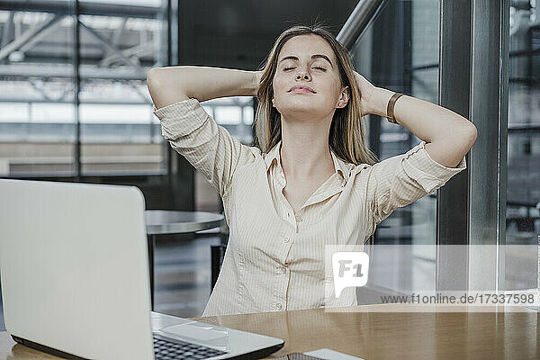 Entspannte Geschäftsfrau sitzt mit den Händen hinter dem Kopf in einem Cafe