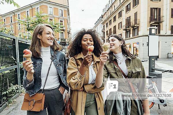 Lächelnde Freunde essen Eis beim Spaziergang in der Stadt