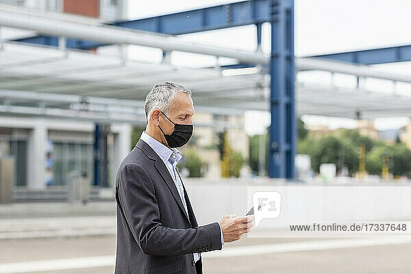 Geschäftsmann benutzt Smartphone am Bahnhof während der Pandemie