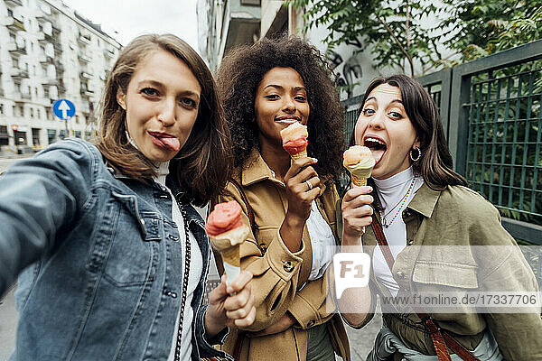 Woman holding ice cream while taking selfie with friends