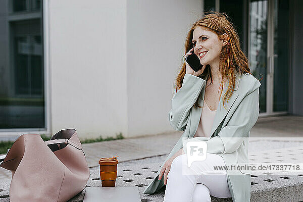 Lächelnde Geschäftsfrau  die auf einer Bank sitzend mit einem Mobiltelefon spricht