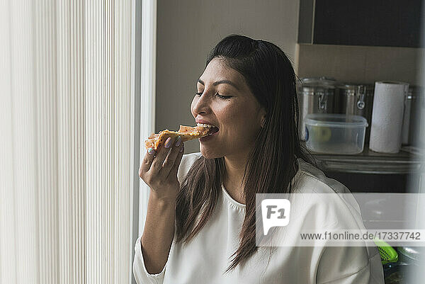 Frau isst Pizza durch einen Vorhang zu Hause