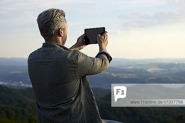 Männlicher Wanderer  der bei Sonnenuntergang durch ein digitales Tablet fotografiert