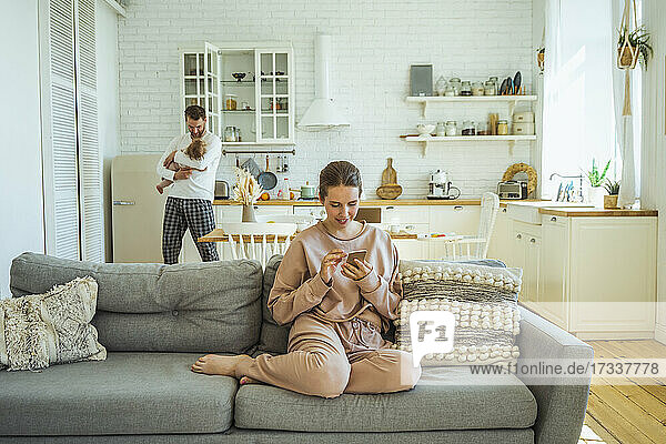 Frau benutzt Mobiltelefon  während Mann seine Tochter zu Hause trägt