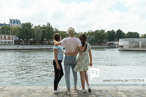 Male and female friends with arms around standing in front of river