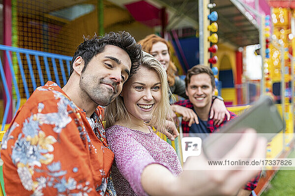 Lächelnde Frau nimmt Selfie mit Freunden durch Smartphone im Vergnügungspark