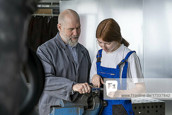 Mature instructor assisting female apprentice working in workshop