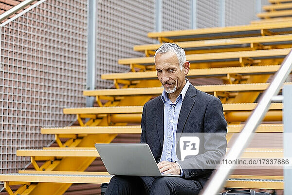 Businessman working on laptop while sitting on staircase