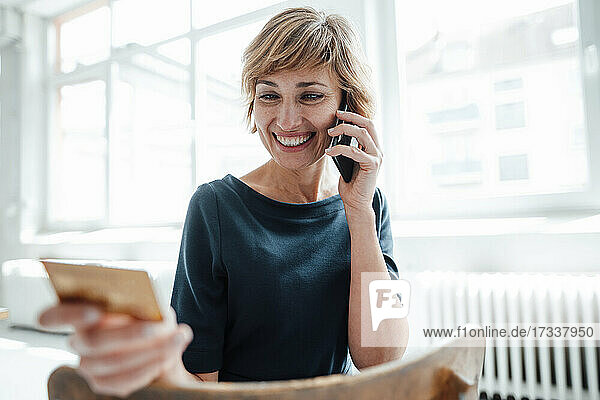 Smiling businesswoman with credit card talking on mobile phone in office