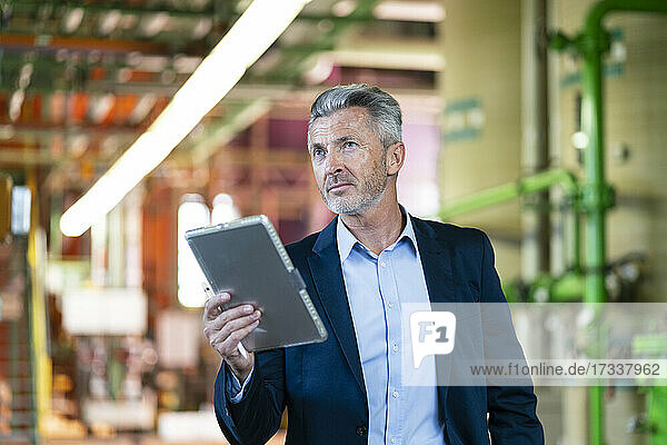 Businessman holding digital tablet while standing in industry