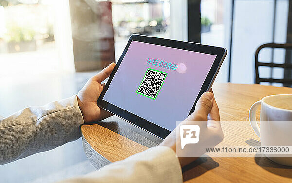 Geschäftsfrau hält digitales Tablet mit QR-Code und Begrüßungstext in einem Café