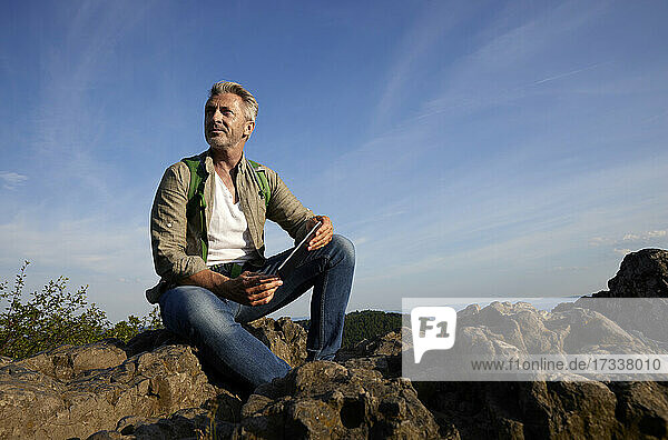 Man with digital tablet sitting on rock