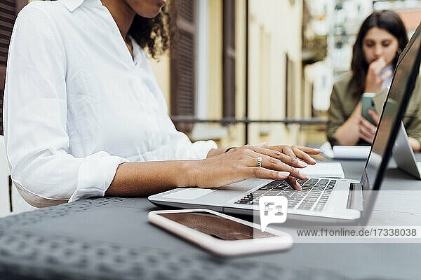 Businesswoman using laptop with colleague in background at terrace