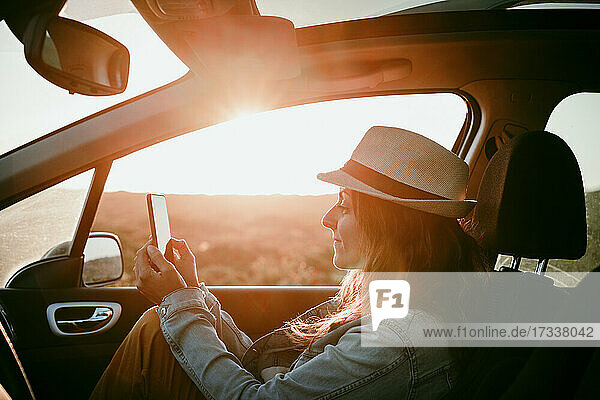 Frau mit Hut  die ein Mobiltelefon benutzt  während sie im Auto sitzt