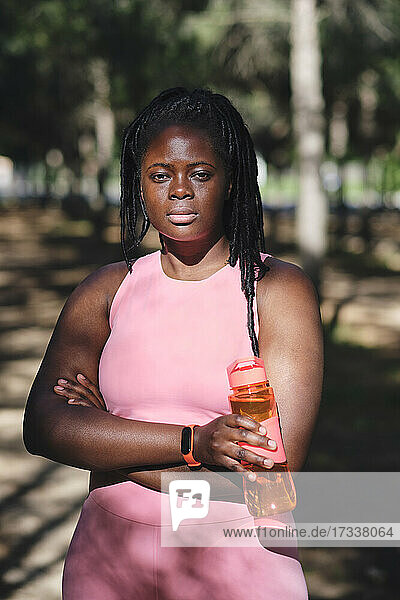 Selbstbewusste junge kurvige Frau mit verschränkten Armen  die eine Wasserflasche hält
