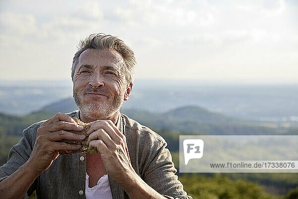Mann lächelt  während er ein Sandwich hält