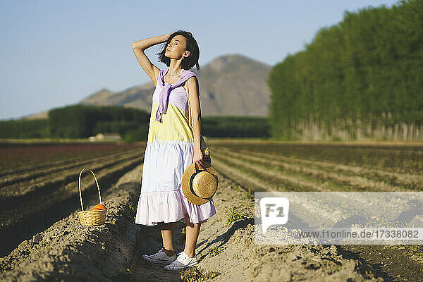 Young woman with eyes closed standing at agricultural field during sunset